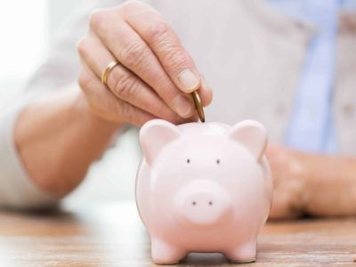 Person inserting a coin into a pink piggy bank, symbolizing savings and financial management.