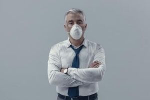 Man in a dusty shirt and mask standing with arms crossed, symbolizing health risks associated with poor indoor air quality from aging ductwork.