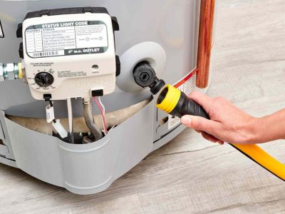 Hand connecting a hose to a water heater for maintenance, showcasing plumbing equipment and status light code panel, emphasizing routine water heater care and efficiency.
