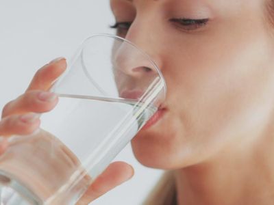 Woman drinking clear water from a glass, emphasizing the benefits of clean and refreshing water from a whole-house water filtration system.