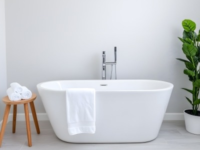 Freestanding bathtub with modern faucet, accompanied by neatly arranged towels on a wooden stool and a potted plant, showcasing a stylish bathroom upgrade.
