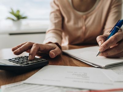 Person using a calculator and writing notes, with paperwork on a table, illustrating financial planning related to energy-efficient home upgrades under the Inflation Reduction Act.