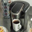 Modern coffee machine dispensing coffee next to pastries and a cup in a cozy kitchen setting.