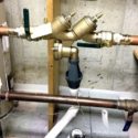 Copper and brass plumbing fixtures with valves and water meter in an industrial setting by PAC Plumbing.