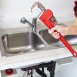 Hand using wrench on dual kitchen sink, showcasing plumbing components for maintenance by PAC Plumbing services.