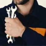 A technician in a work uniform holds three wrenches, ready for plumbing maintenance and HVAC services.
