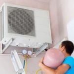 Person working on a wall-mounted air conditioning unit with a pink refrigerant tank for PAC HVAC services.