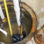 Sump pump next to PVC pipes with measurement tape, showing water accumulation in a basement managed by PAC Plumbing.