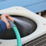 Close-up of air conditioning unit being cleaned with water spray by a technician from PAC HVAC services.