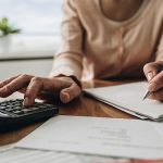 Close-up of hands using a calculator and notes in a calm workspace, reflecting productivity for HVAC and plumbing services.