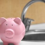 Pink piggy bank on a kitchen counter, with a coin slot, adjacent to a kitchen sink.