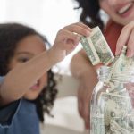 Child adding dollar bills to a jar, with an adult smiling, symbolizing financial literacy education by PAC Plumbing.