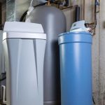 Water filtration system components: gray and blue tanks with a white filtration unit in an industrial setting.