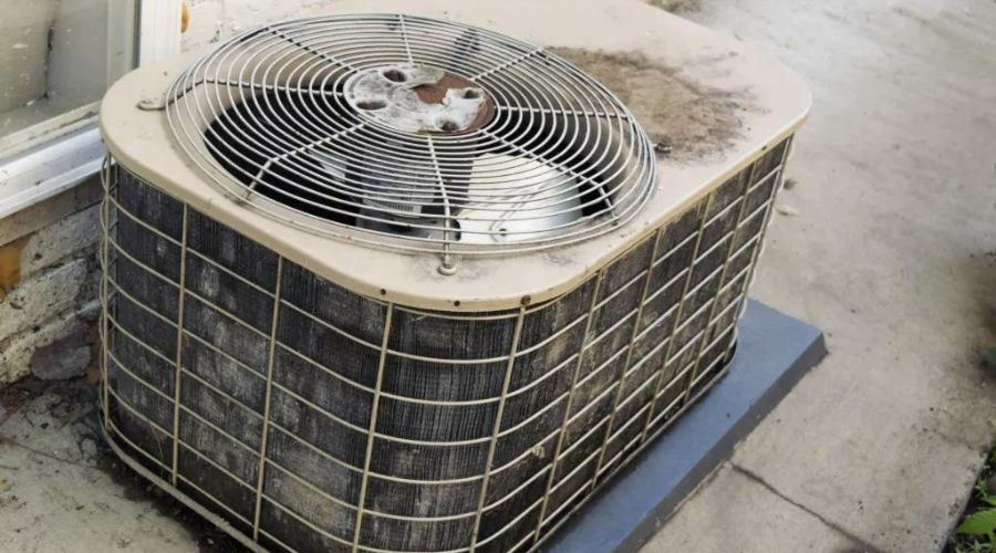 Dusty air conditioning unit with visible wear, placed next to a building on concrete, representing HVAC service needs.