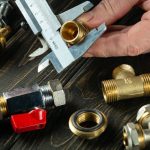 Hand holding a caliper measuring brass plumbing fittings on a wooden surface, highlighting PAC Plumbing's precision.