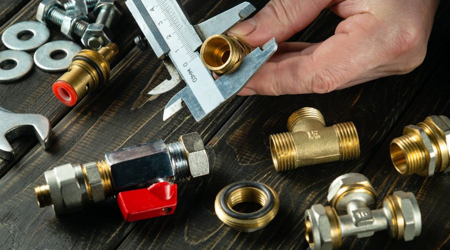 Close-up of plumbing fittings, including brass valves and measuring tools, on a wooden surface at PAC Plumbing.
