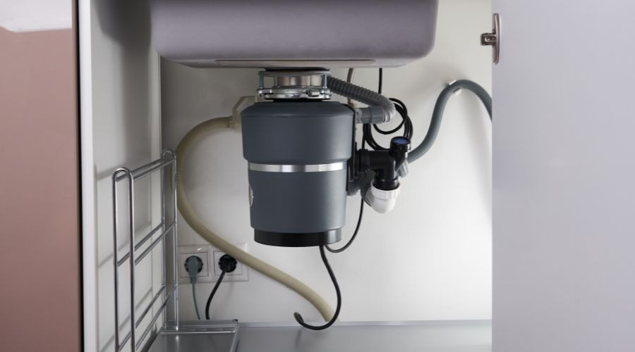 Garbage disposal unit under kitchen sink with plumbing connections, by PAC Plumbing, Heating, and Air Conditioning.