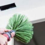 Person using a green duct cleaning brush to clean air ducts, emphasizing the importance of professional duct cleaning for HVAC efficiency and indoor air quality.