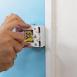 Hand installing a smart thermostat on a blue wall, illustrating the process of upgrading to modern HVAC technology for improved energy efficiency and comfort management.